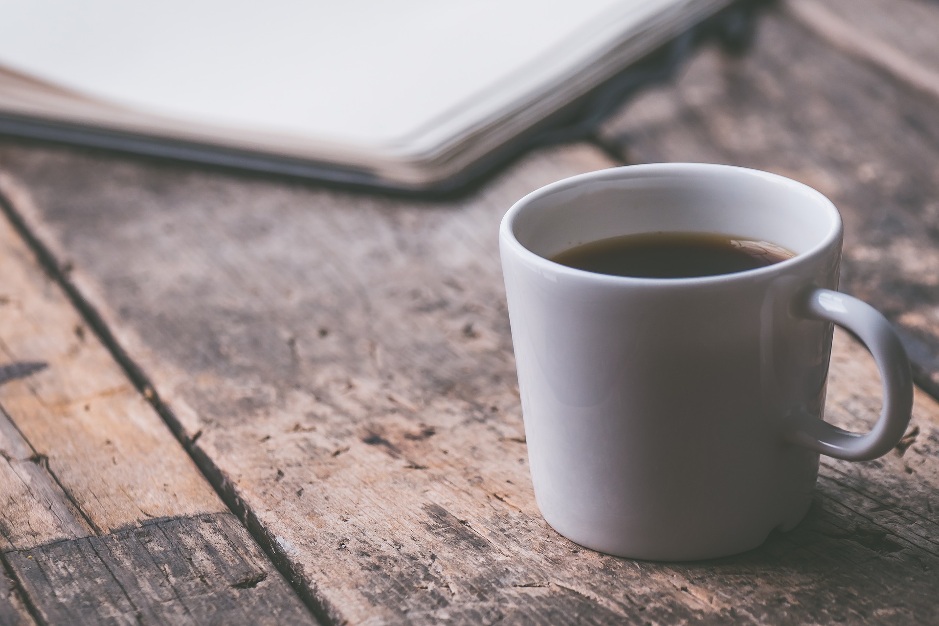 Tasse Kaffee und im Hintergrund ein Schreibblock auf Holztisch